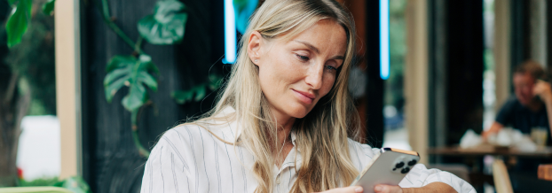 Symbolbild für den Pressekontakt. Eine Frau sitzt im Cafe und liest Nachrichten auf Ihrem Smartphone.